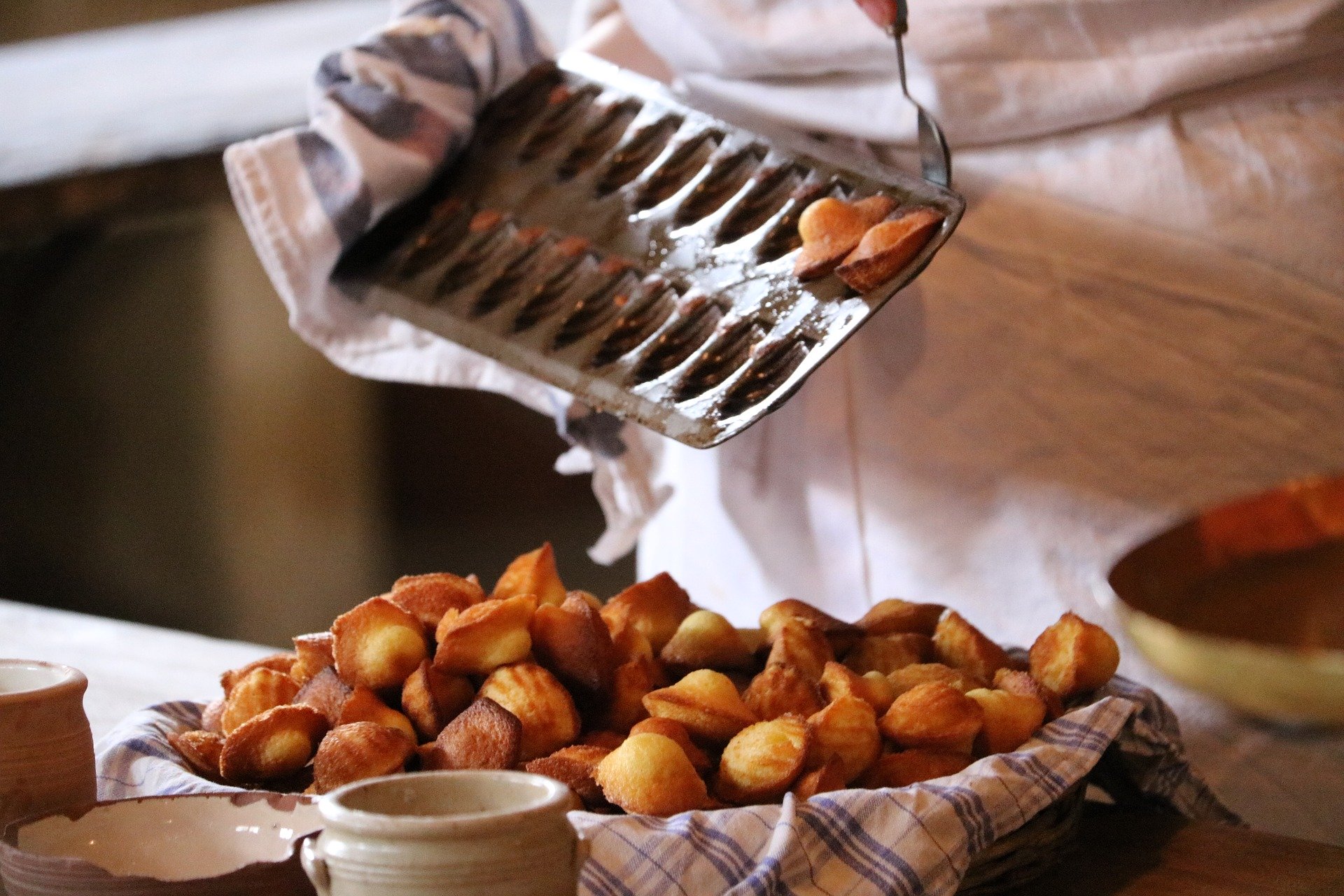 Personne avec un tablier blanc qui démoule des madeleines avec une cuillère